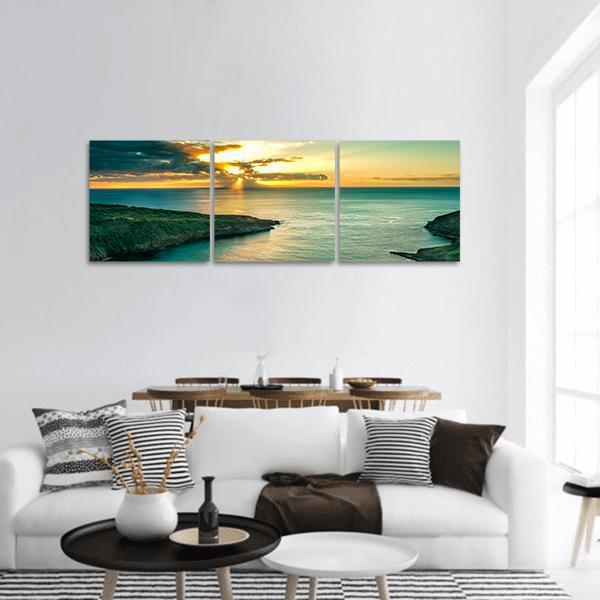 Sunrise Over Coastal Cliffs and Calm Water Panoramic Canvas Wall Art in orange, yellow and blue, hung on a wall