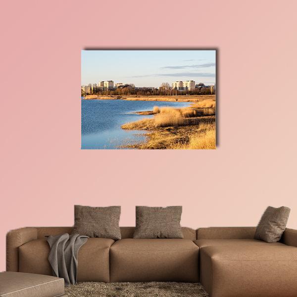 Lake with Golden Reeds and Distant Buildings Canvas Wall Art in beige, gold and blue, single panel hung on a wall