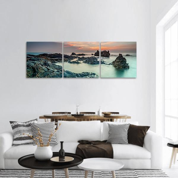 Sunrise Over Rocky Shore Panoramic Canvas Wall Art in gray, orange and blue, hung on a wall