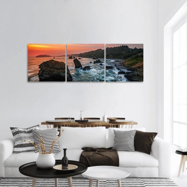 Rocky Beach at Sunset with Sea Stack Panoramic Canvas Wall Art in brown, orange and blue, hung on a wall