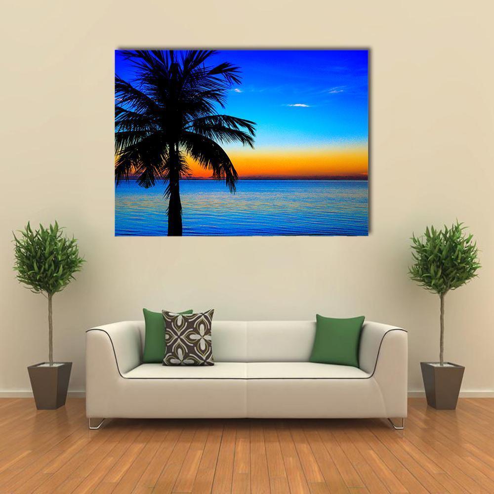 Palm Tree Sunset Over Sea Canvas Wall Art in orange, yellow and blue, single panel hung on a wall
