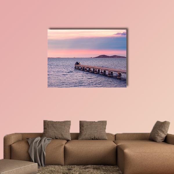 Two Silhouettes on a Jetty at Sunset Canvas Wall Art in blue, purple and pink, single panel hung on a wall
