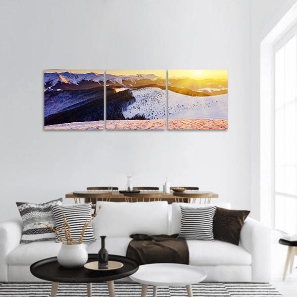 Sunset Over Snowy Mountain Peaks Panoramic Canvas Wall Art in white, orange and blue, hung on a wall