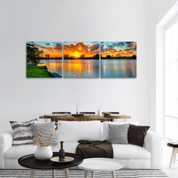 Golden Sunset Over Calm Lake Panoramic Canvas Wall Art in orange, yellow and blue, hung on a wall
