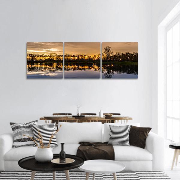 Sunset Over Small Lake Panoramic Canvas Wall Art in orange, yellow and blue, hung on a wall