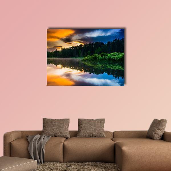Sunset Sky Over Reflective Pond Canvas Wall Art in orange, green and blue, single panel hung on a wall
