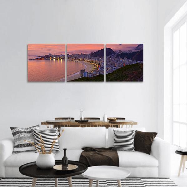 Sunset Over Curved Coastline Panoramic Canvas Wall Art in orange, purple and pink, hung on a wall