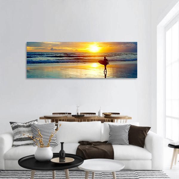 Surfer on Beach at Sunset Panoramic Canvas Wall Art in orange, yellow and blue, hung on a wall
