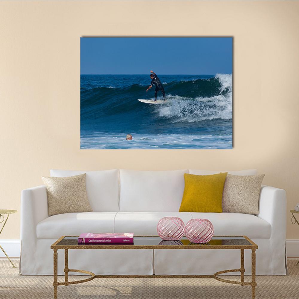 Surfers Riding Ocean Waves Canvas Wall Art in white and blue, single panel hung on a wall