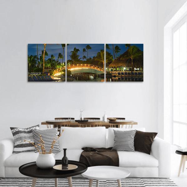 Nightlit Resort Pool with Glowing Bridge Panoramic Canvas Wall Art in black, yellow and blue, hung on a wall