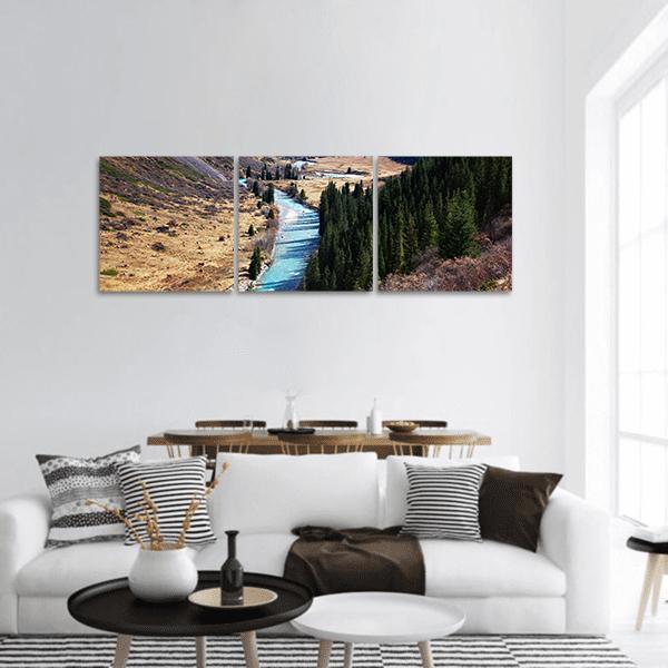 Mountain Valley with Turquoise River Panoramic Canvas Wall Art in brown, green and blue, hung on a wall