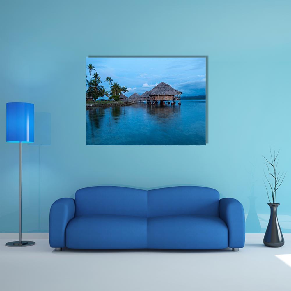 Overwater Bungalows in Blue Water Canvas Wall Art in blue, single panel hung on a wall