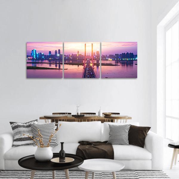 Cable-stayed Bridge at Dusk with City Skyline Panoramic Canvas Wall Art in blue, purple and pink, hung on a wall