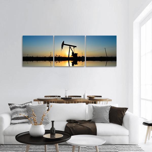 Oil Pump Jack with Water Reflection Panoramic Canvas Wall Art in black, orange and blue, hung on a wall