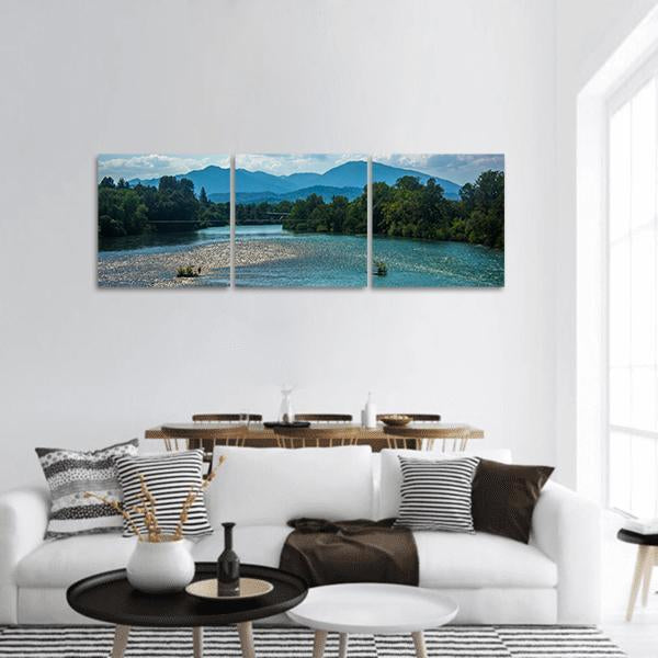 Shallow River with Layered Blue Mountains Panoramic Canvas Wall Art in green and blue, hung on a wall