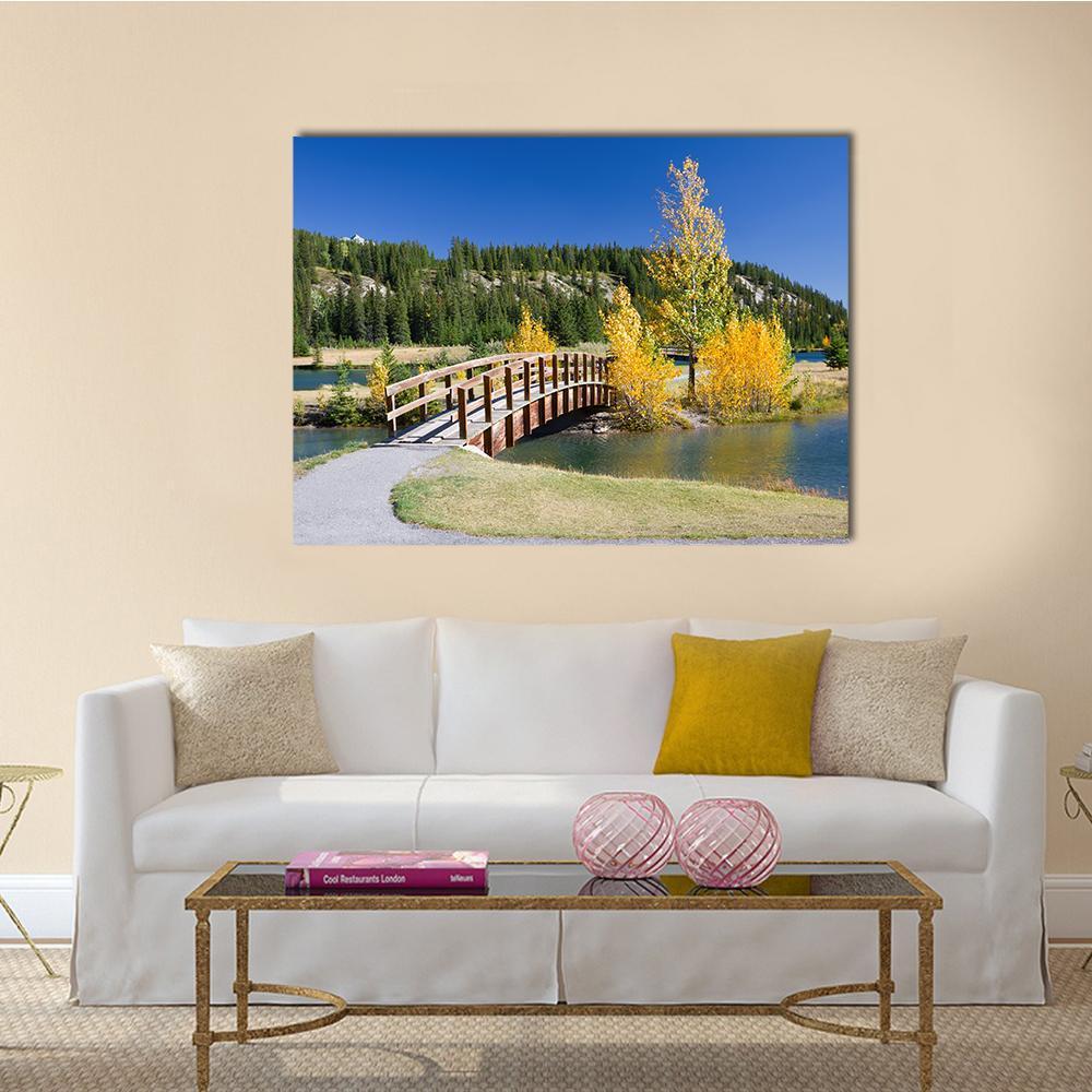Banff National Park Autumn Footbridge Canvas Wall Art in yellow, green and blue, single panel hung on a wall