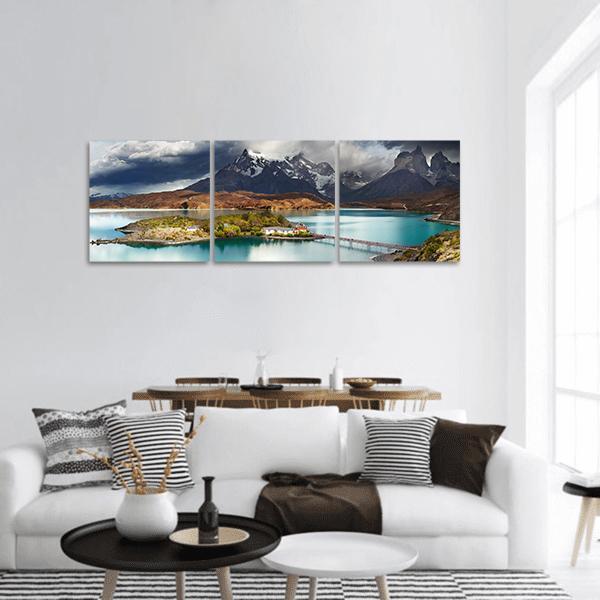 Lake Pehoe with Island and Wooden Bridge Panoramic Canvas Wall Art in gray, brown and blue, hung on a wall