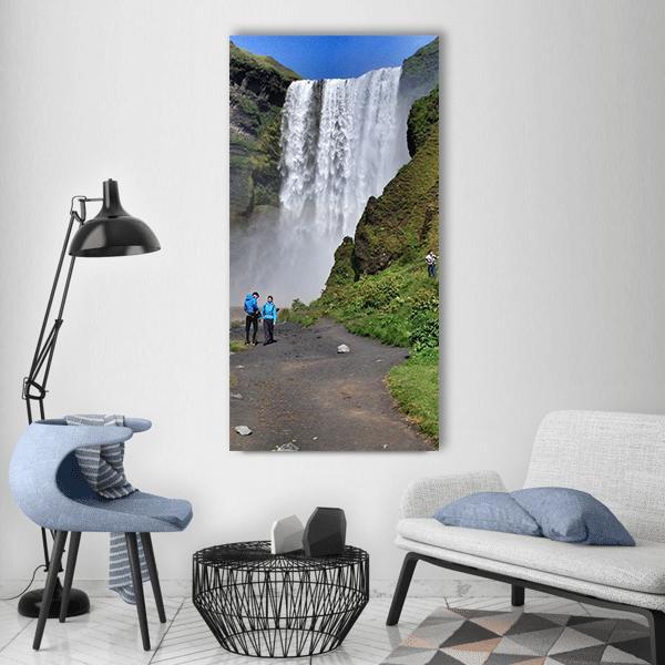 Tourists Near Waterfall in Iceland Vertical Canvas Wall Art in white, green and blue, single vertical panel hung on a wall