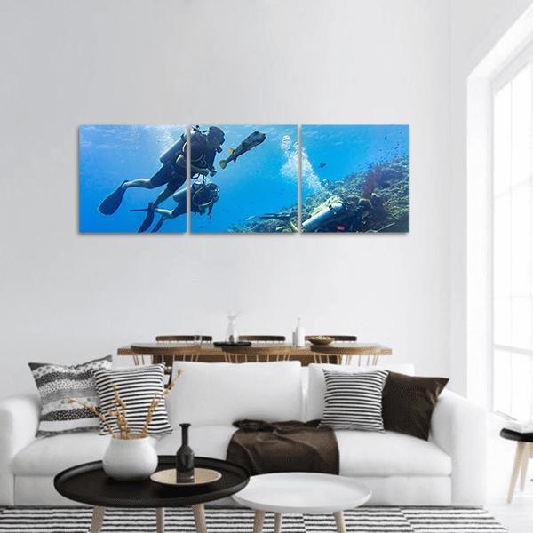 Scuba Divers at Coral Reef Panoramic Canvas Wall Art in blue, hung on a wall