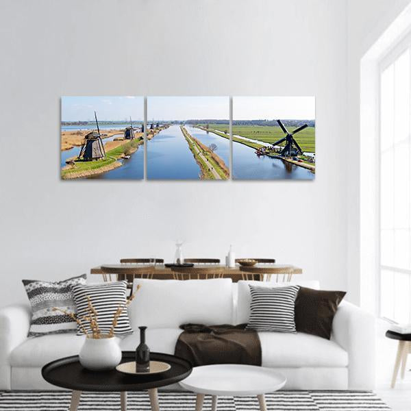 Dutch Windmills Along a Canal Panoramic Canvas Wall Art in white, green and blue, hung on a wall