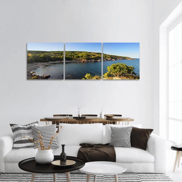 Tranquil Coastal Bay with Sandy Cove Panoramic Canvas Wall Art in green and blue, hung on a wall