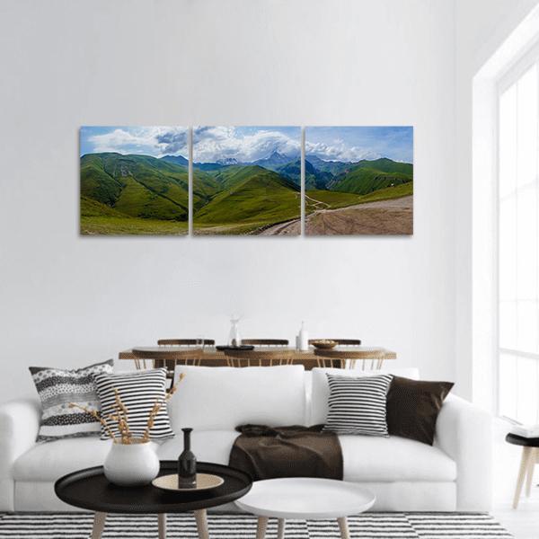 Winding Dirt Road Through Green Mountains Panoramic Canvas Wall Art in brown, green and blue, hung on a wall
