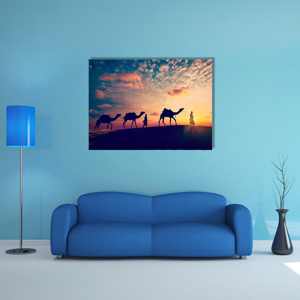 Two Cameleers Crossing Desert Dunes Canvas Wall Art in orange, yellow and blue, single panel hung on a wall