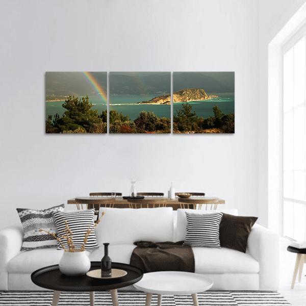 Rainbow Over Coastal Island and Forested Hills Panoramic Canvas Wall Art in gray, green and blue, hung on a wall
