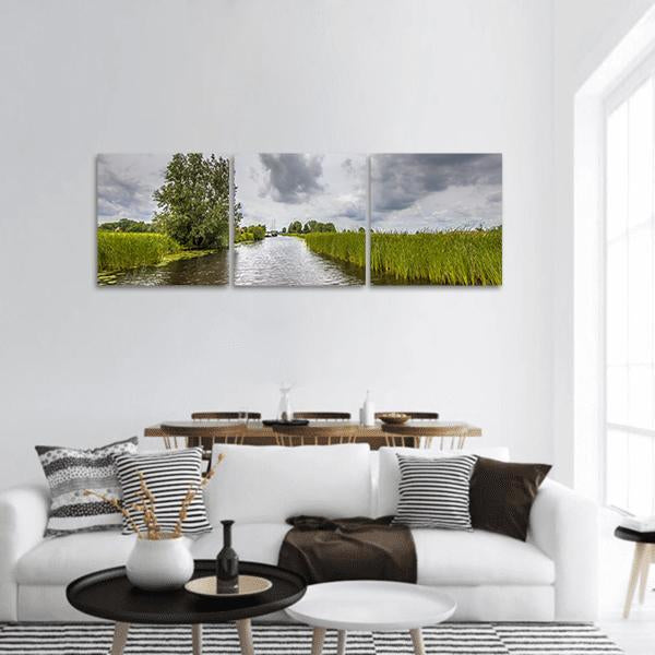 Canal View with Tall Reeds and Boat Panoramic Canvas Wall Art in white, gray and green, hung on a wall