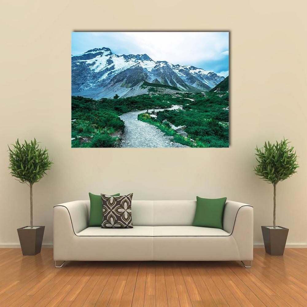 Snow-capped Peaks with Winding Trail and Stream Canvas Wall Art in white, green and blue, single panel hung on a wall