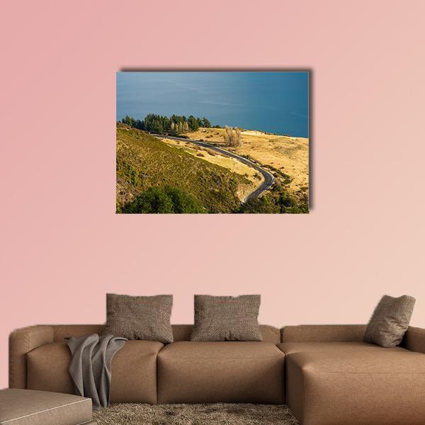 Winding Road Along Mountain Lake Canvas Wall Art in yellow, green and blue, single panel hung on a wall