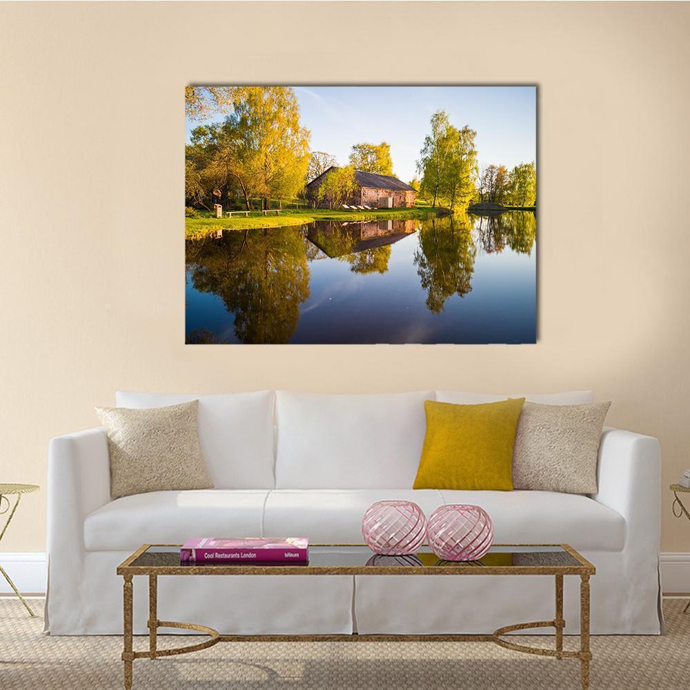 Brick Barn and Tree Reflection on Lake Canvas Wall Art in yellow, green and blue, single panel hung on a wall