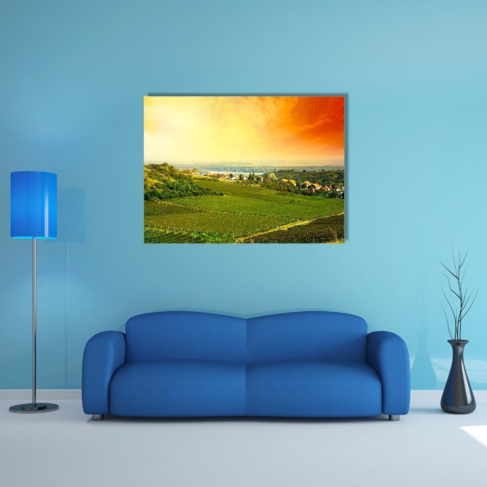 Sunset Over Vineyard and Village Canvas Wall Art in orange, yellow and green, single panel hung on a wall