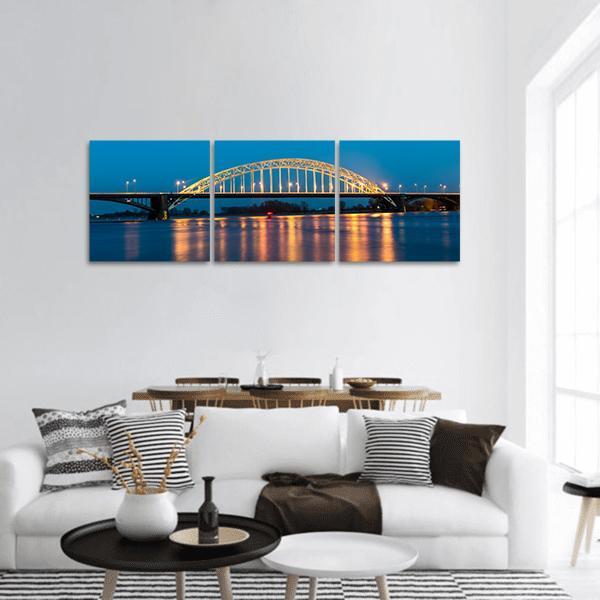 Waal Bridge at Nijmegen Night Reflections Panoramic Canvas Wall Art in black, yellow and blue, hung on a wall