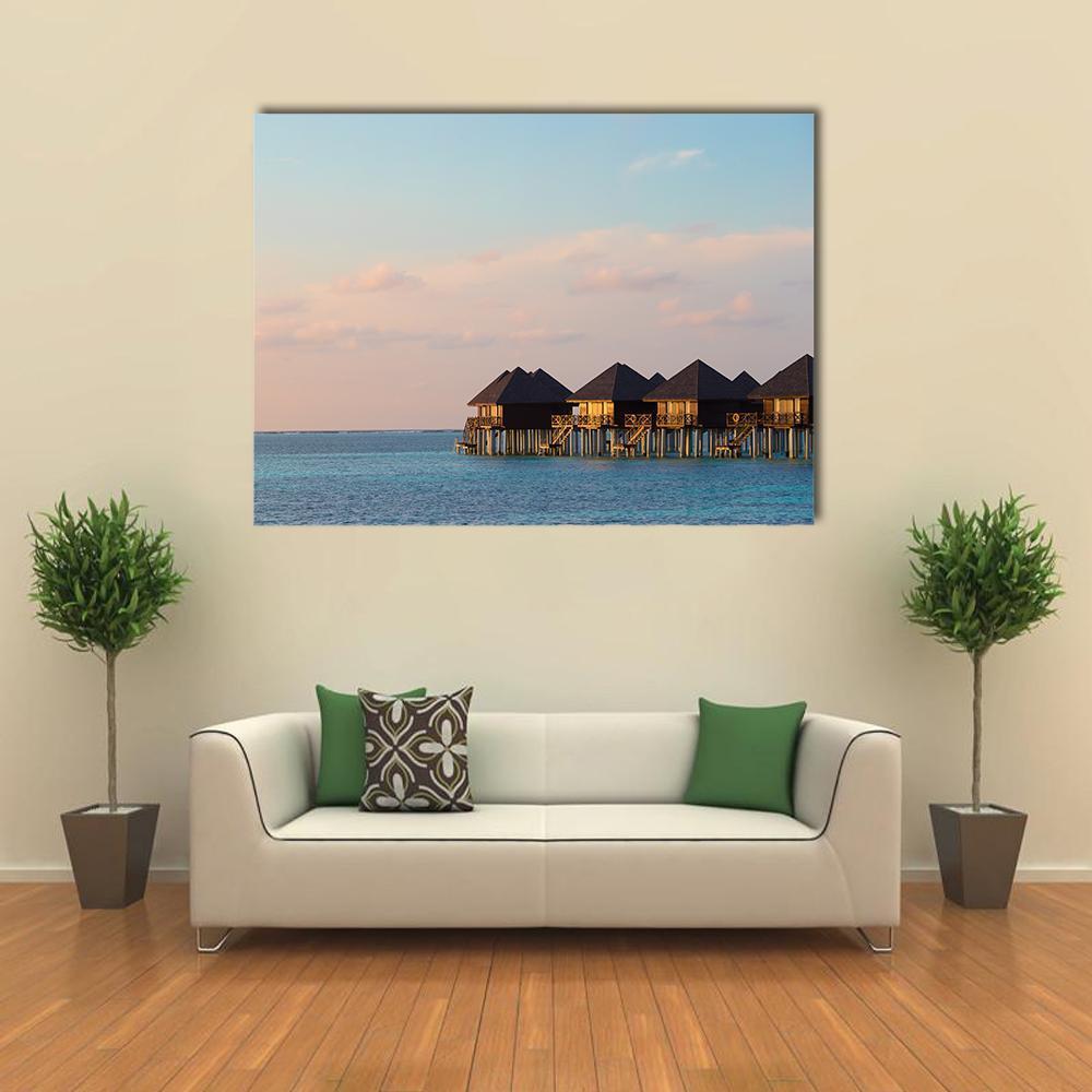 Tropical Overwater Bungalows at Sunset Canvas Wall Art in orange, blue and pink, single panel hung on a wall