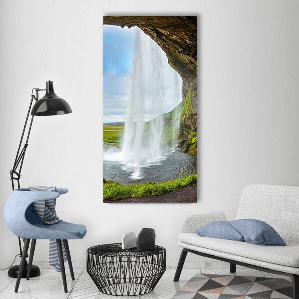 Waterfall Above a Cave Vertical Canvas Wall Art in white, brown and green, single vertical panel hung on a wall