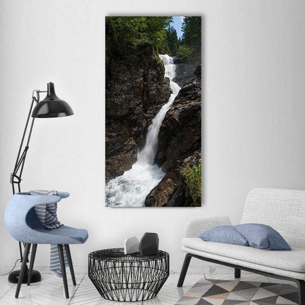 Alpine Waterfall with Craggy Rocks Vertical Canvas Wall Art in white, gray and green, single vertical panel hung on a wall