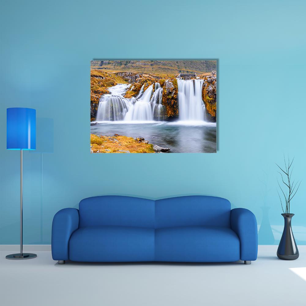 Autumn Waterfall with Wooden Bridge Canvas Wall Art in brown, orange and blue, single panel hung on a wall