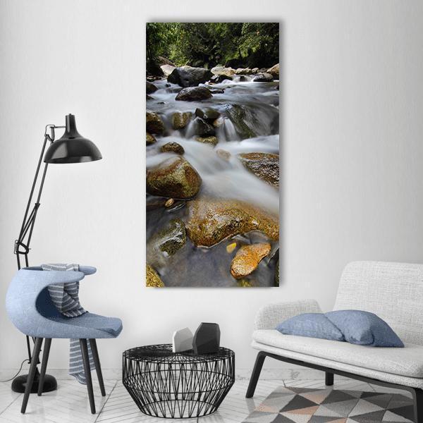 Green Waterfall Over Rocks and Forest Vertical Canvas Wall Art in gray, brown and green, single vertical panel hung on a wall