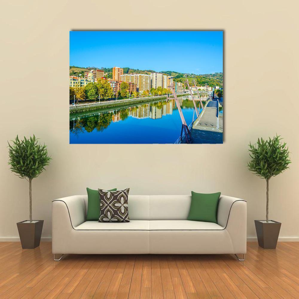 Autumn Riverfront with Bridge Reflection Canvas Wall Art in yellow, green and blue, single panel hung on a wall