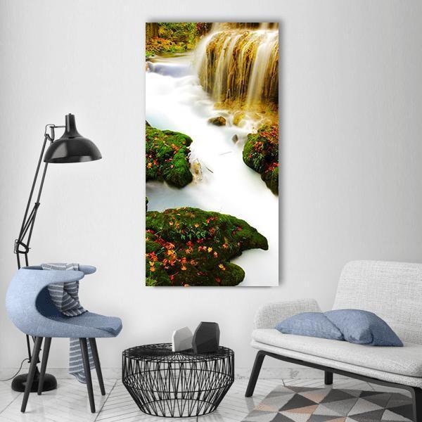 Waterfall with Mossy Rocks and Autumn Leaves Vertical Canvas Wall Art in white, orange and green, single vertical panel hung on a wall