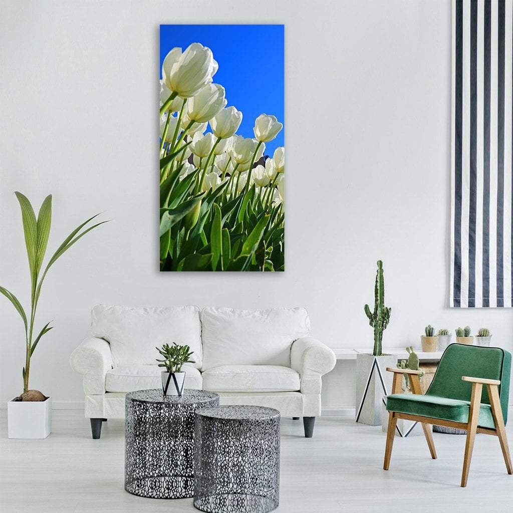White Tulips Against Blue Sky Vertical Canvas Wall Art in white, green and blue, single vertical panel hung on a wall