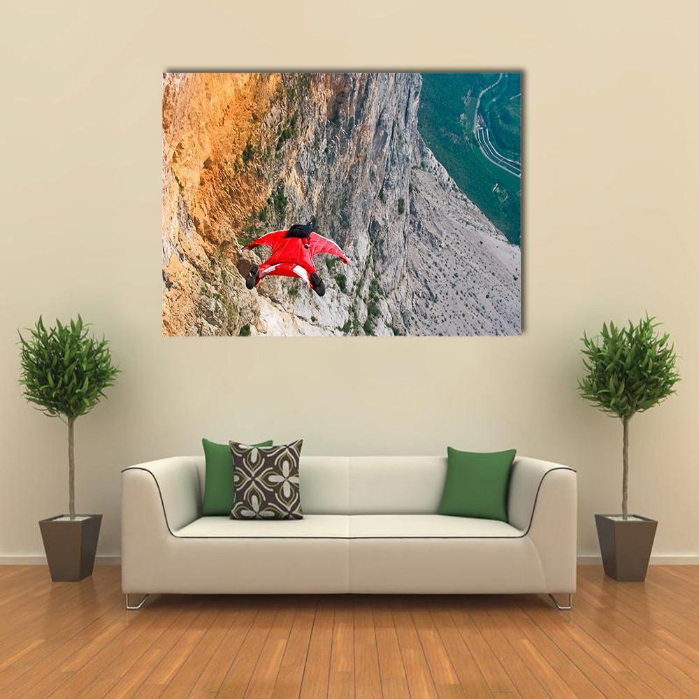 Wingsuit Flyer Jumping from Mountain Cliff Canvas Wall Art in gray, orange and green, single panel hung on a wall