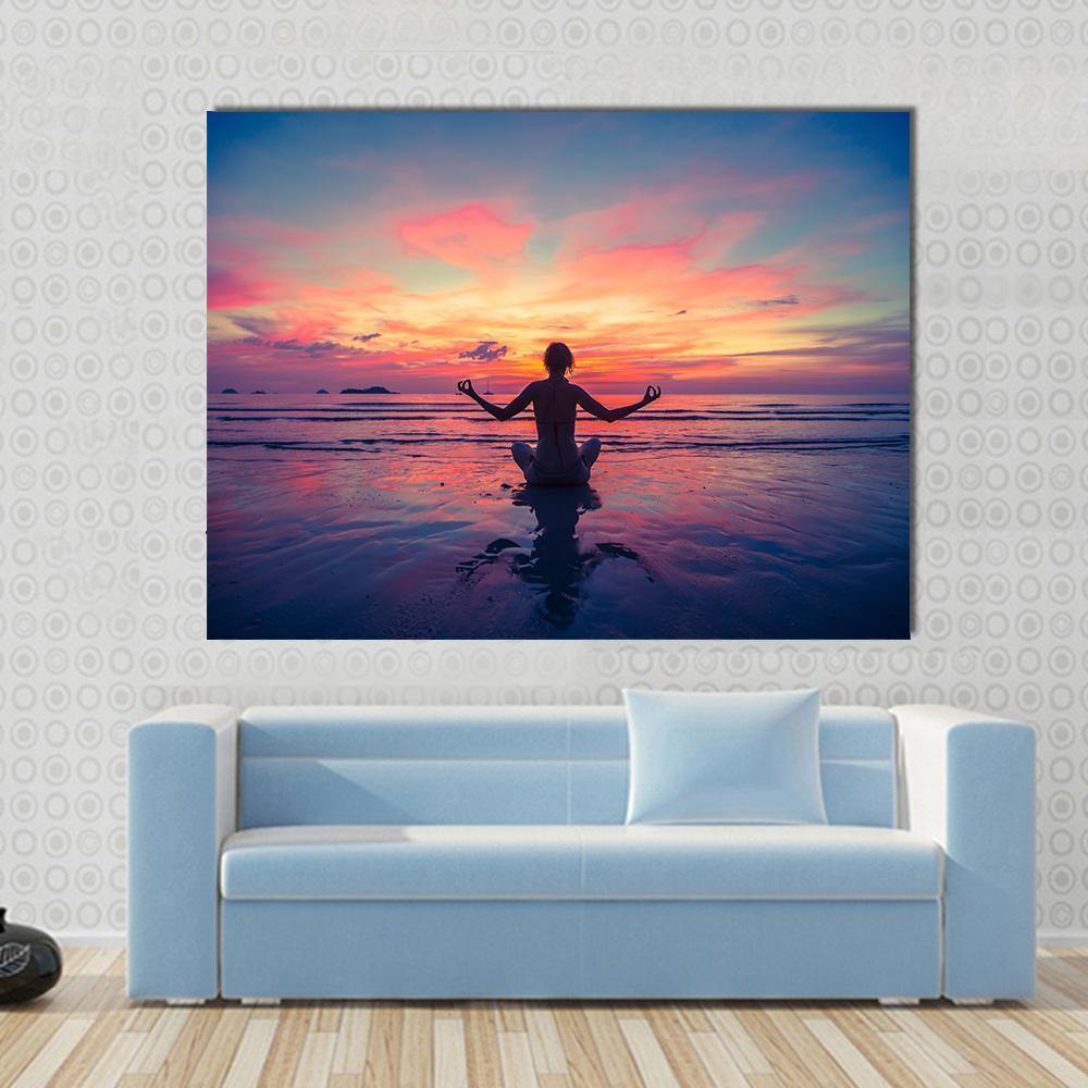 Woman Meditating on Ocean Beach at Sunset Canvas Wall Art in orange, blue and pink, single panel hung on a wall