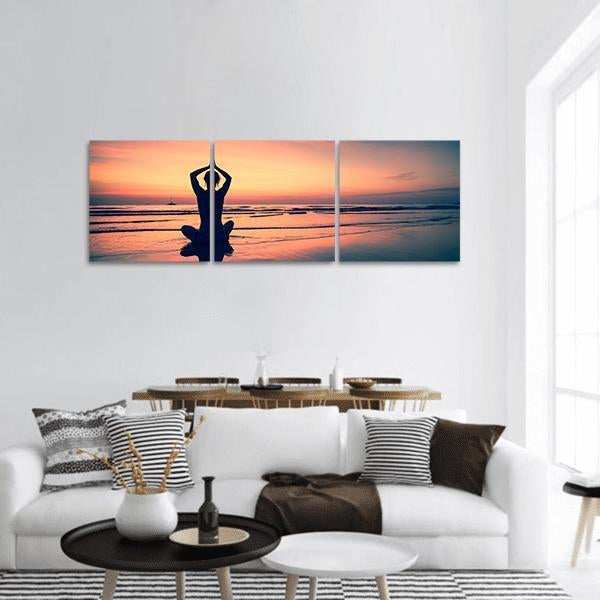 Woman Meditating on Beach at Sunset Panoramic Canvas Wall Art in orange, blue and pink, hung on a wall