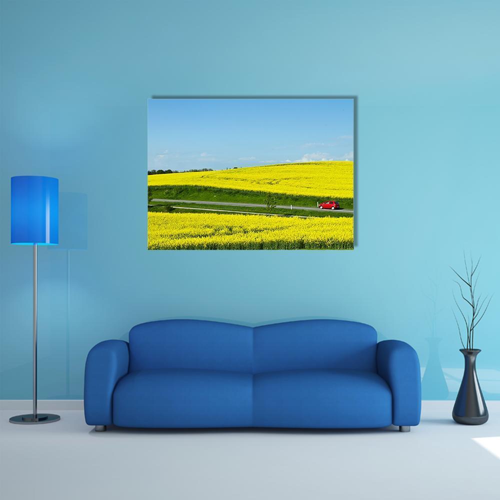 Red Car on Road Through Yellow Field Canvas Wall Art in yellow, green and blue, single panel hung on a wall