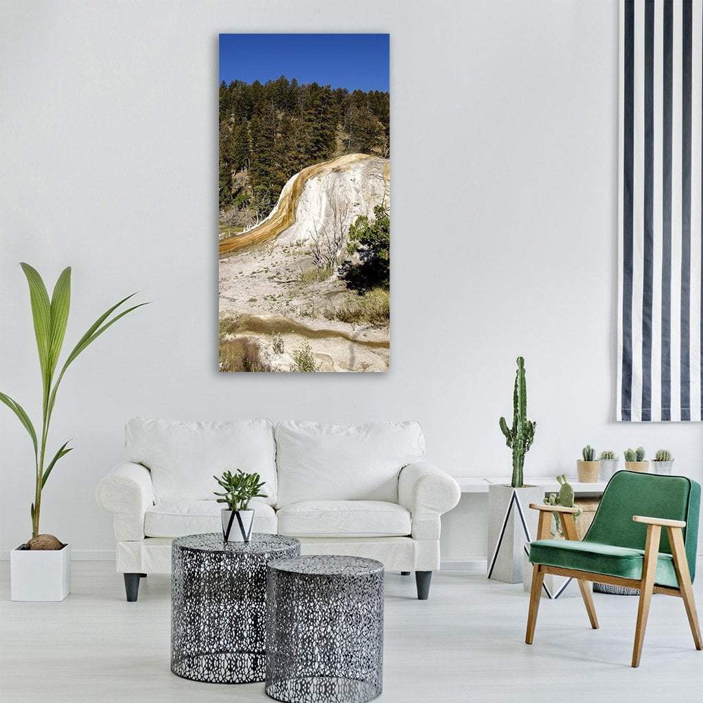 Yellowstone Travertine Terrace and Pine Forest Vertical Canvas Wall Art in beige, brown and blue, single vertical panel hung on a wall