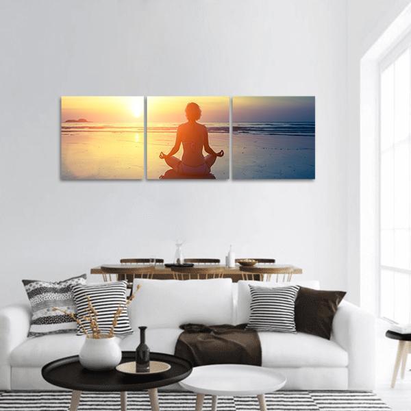 Woman Meditating at Sunset Beach Panoramic Canvas Wall Art in orange, yellow and blue, hung on a wall